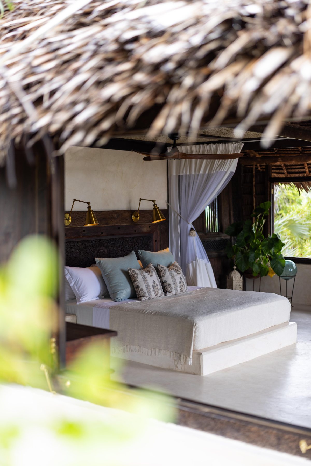 Aloha cabana, netted bed with brass lamps and a carved headboard beneath the makuti thatch