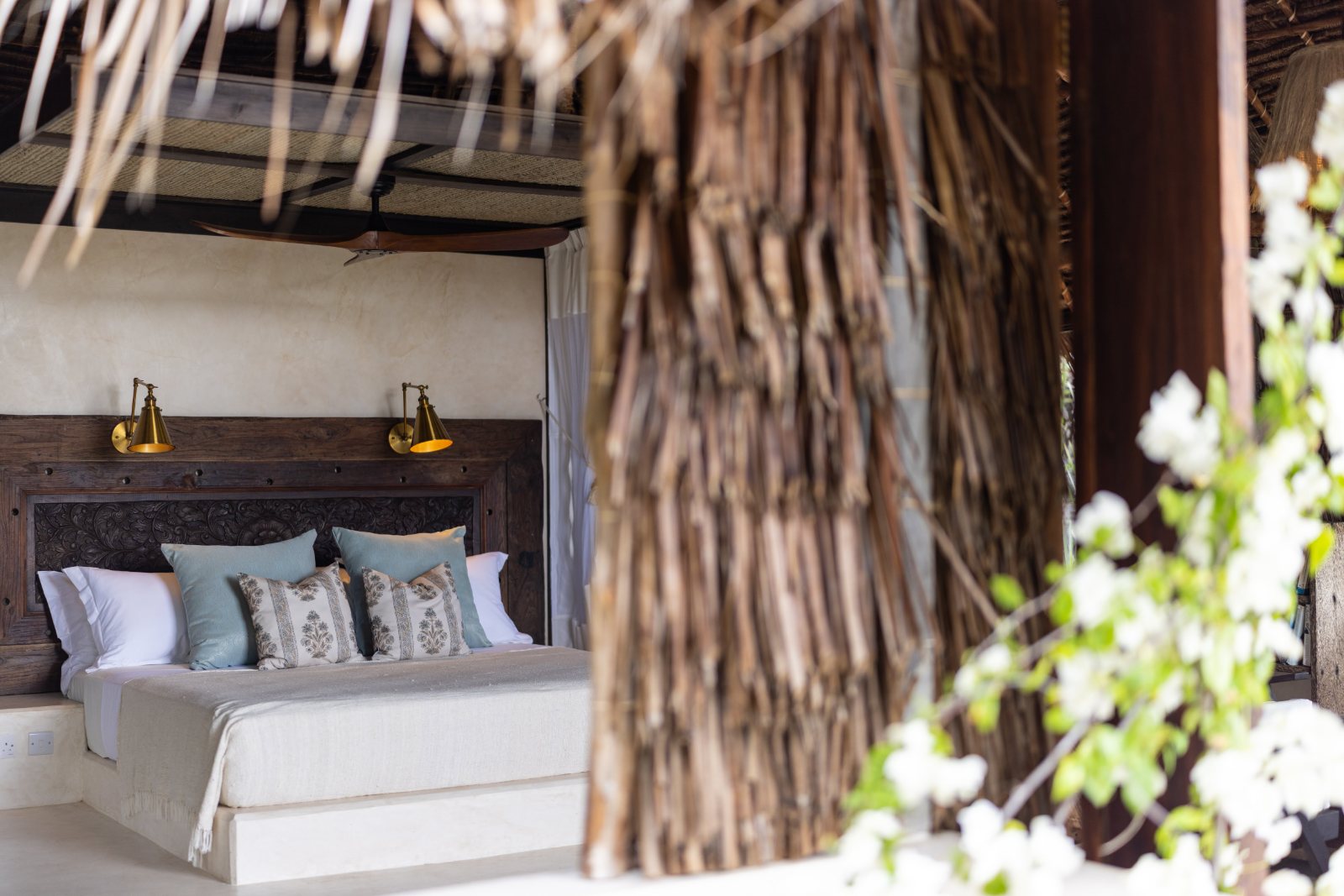 Aloha cabana, bed framed by a makuti thatch column with bougainvillea in flower