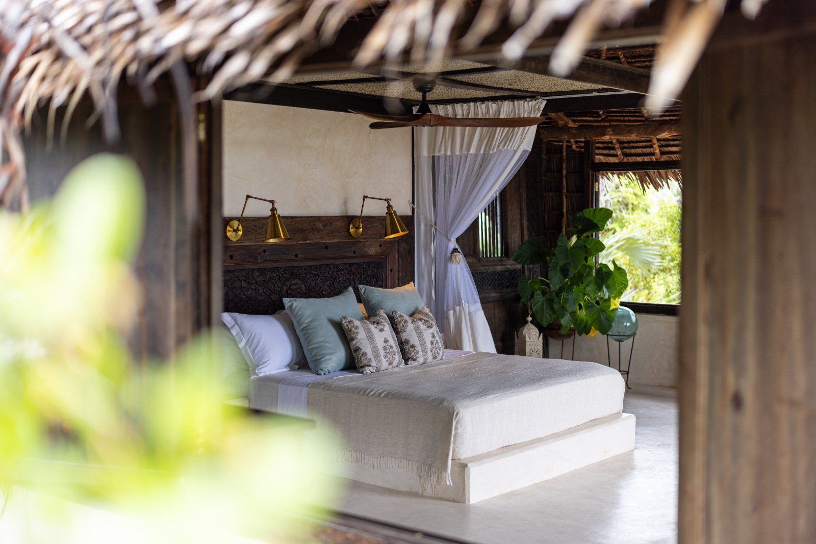 Aloha cabana, carved headboard, brass reading lamps and drifting mosquito net open to the garden