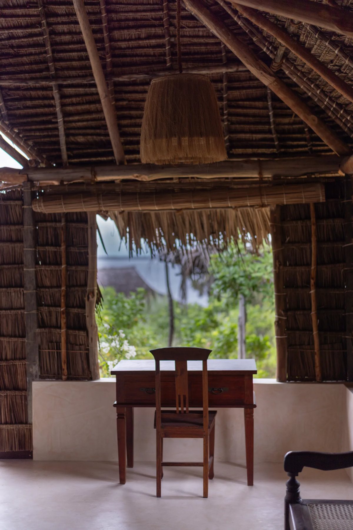 Aloha cabana · the desk nook framed by palm thatch, looking out to the trees