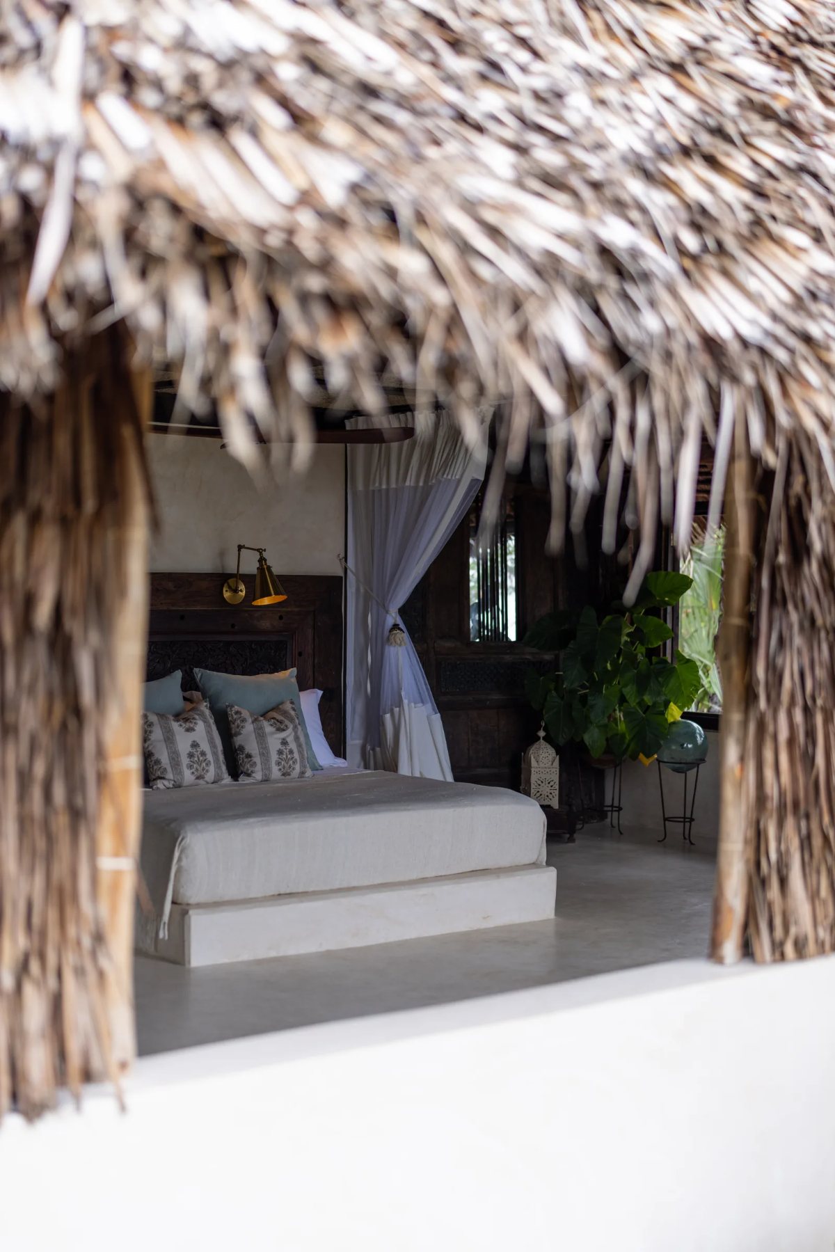 Aloha cabana · the bed glimpsed through the makuti eaves from the veranda