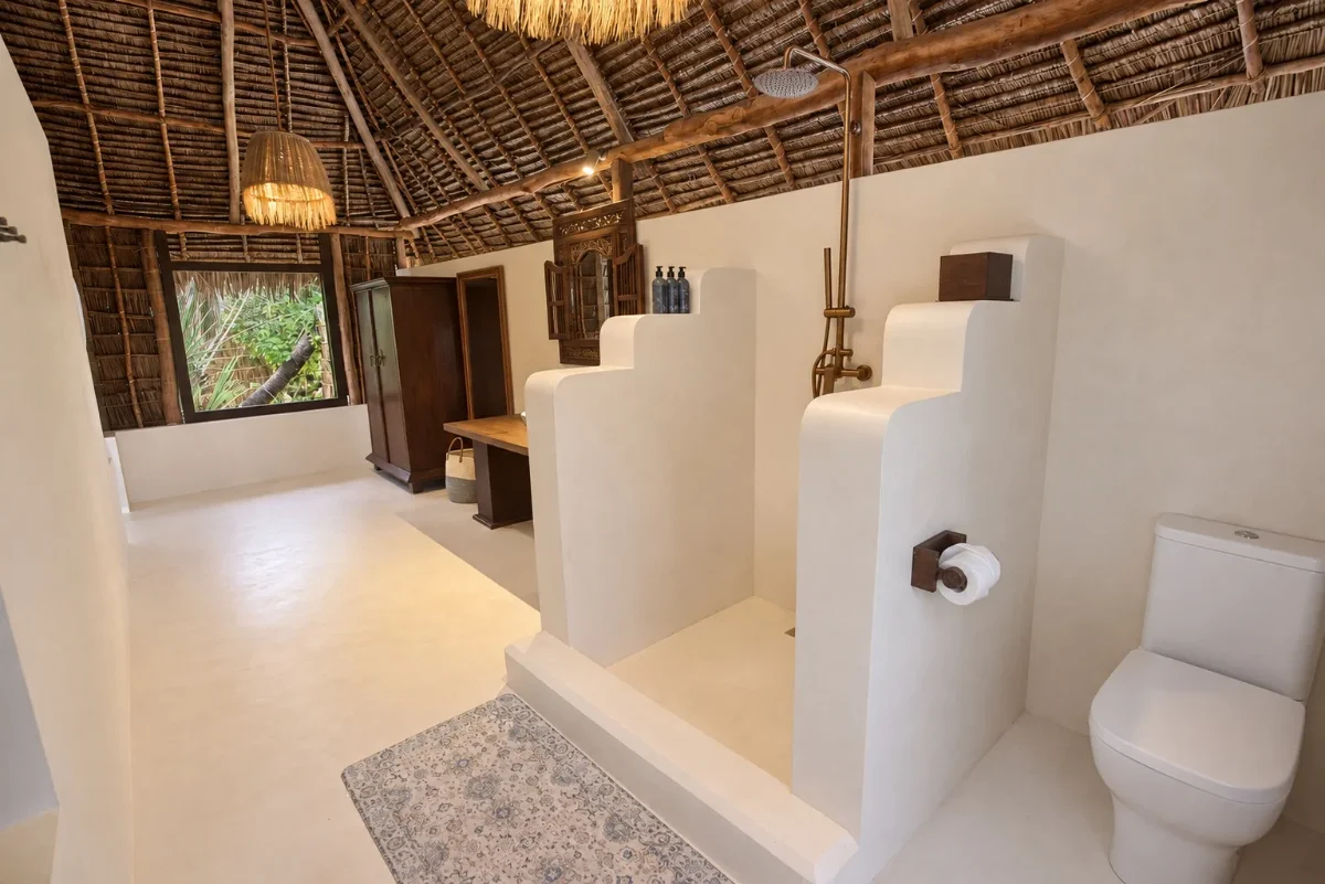 The Aloha ensuite, a sculpted lime-plaster shower under the makuti roof