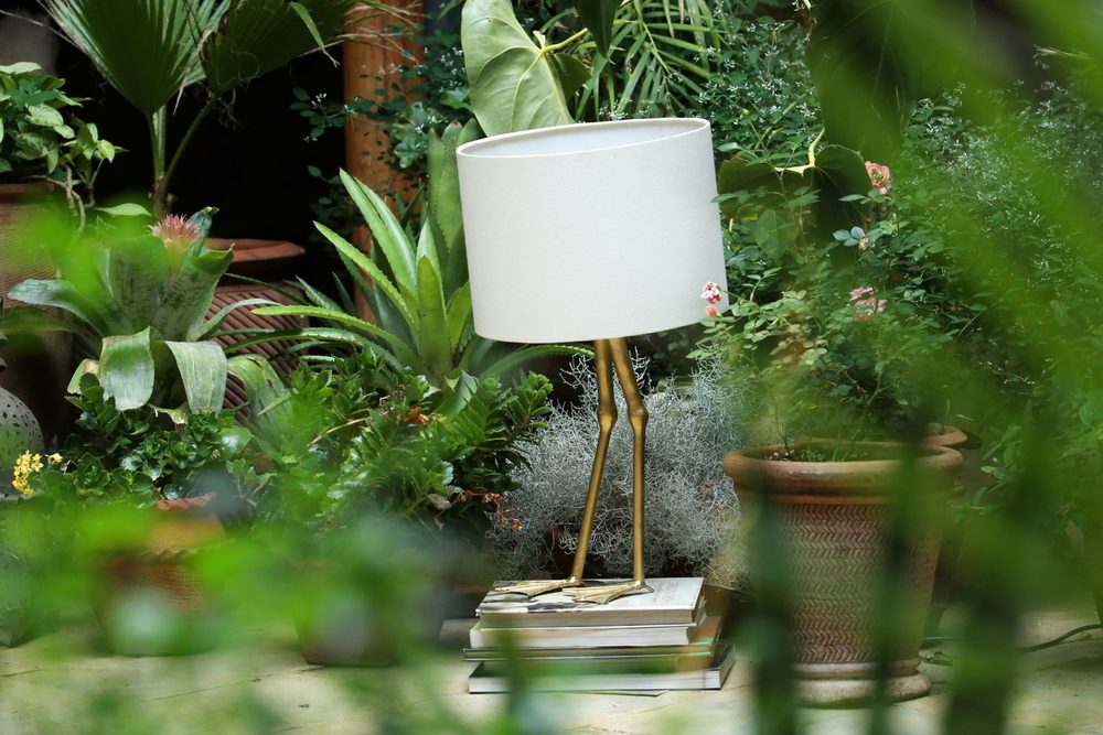 The brass crane-leg lamp from another angle, framed by ferns and Spanish moss