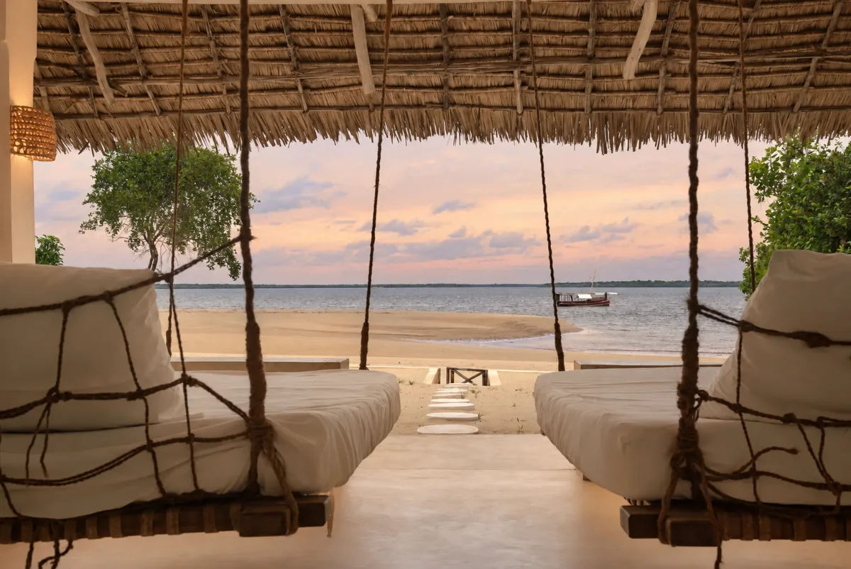 Makai ground floor, two hanging swing beds framing the beach, the channel and a moored dhow