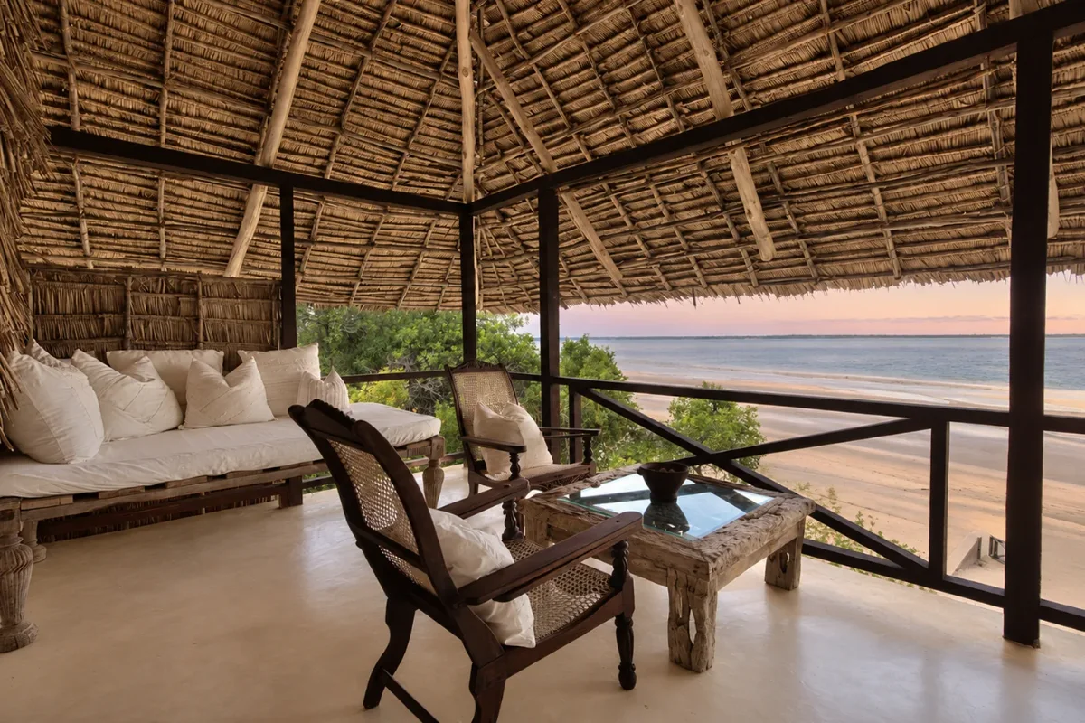 Makai first-floor verandah, planter chairs and a daybed above the beach at sunset