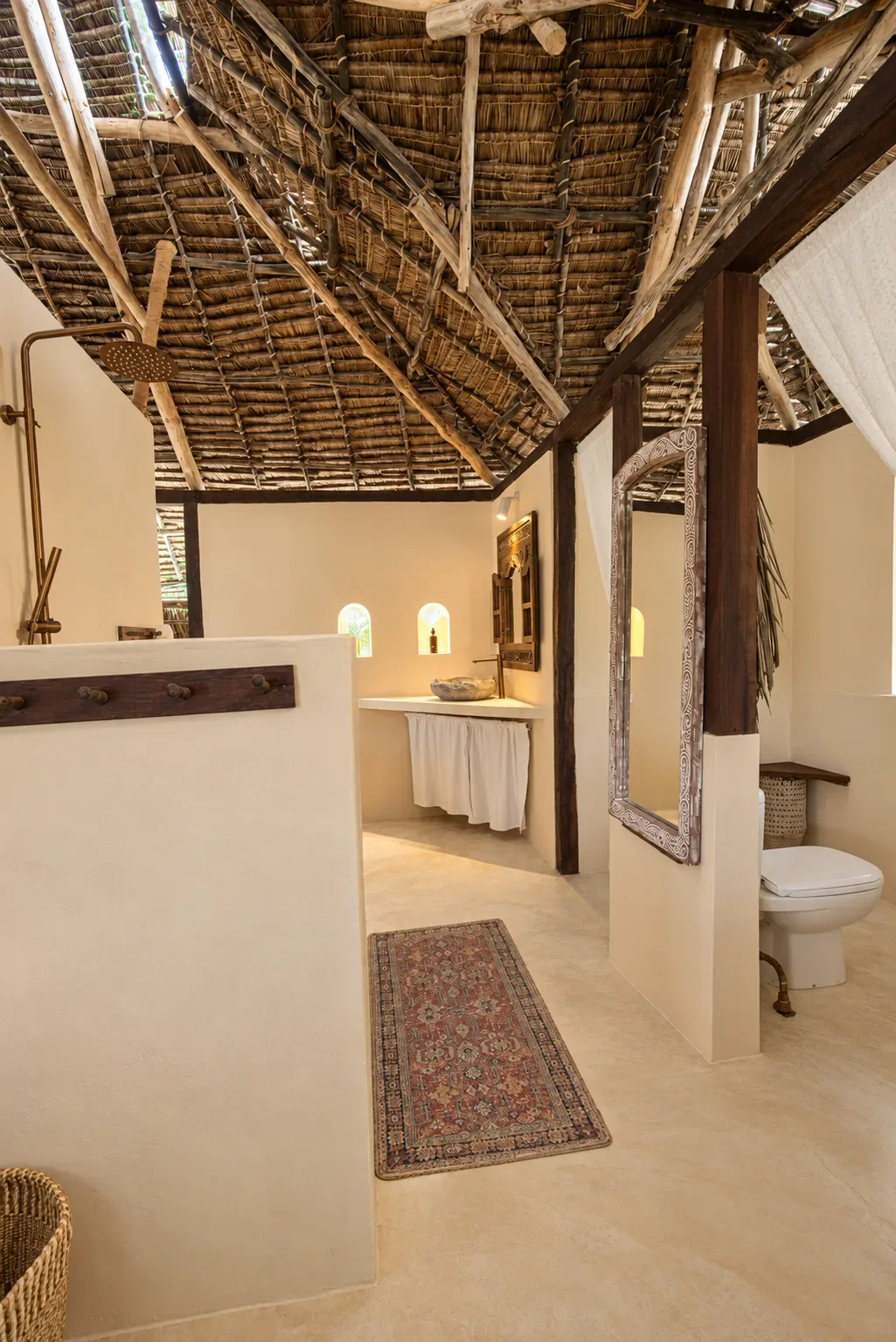 Makai first-floor bathroom under the thatch, rain shower, stone basin and a carved mirror