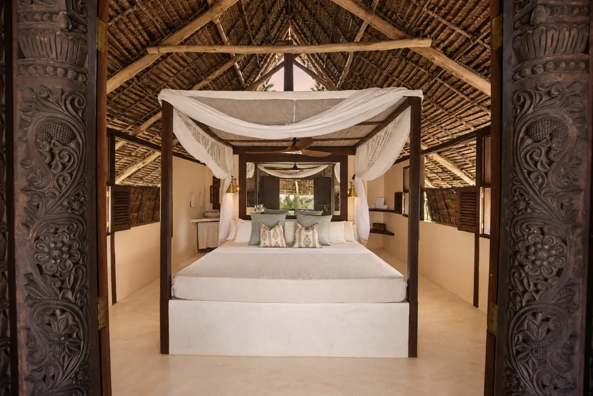 Makai first-floor bedroom seen through carved doors, the four-poster beneath the thatch