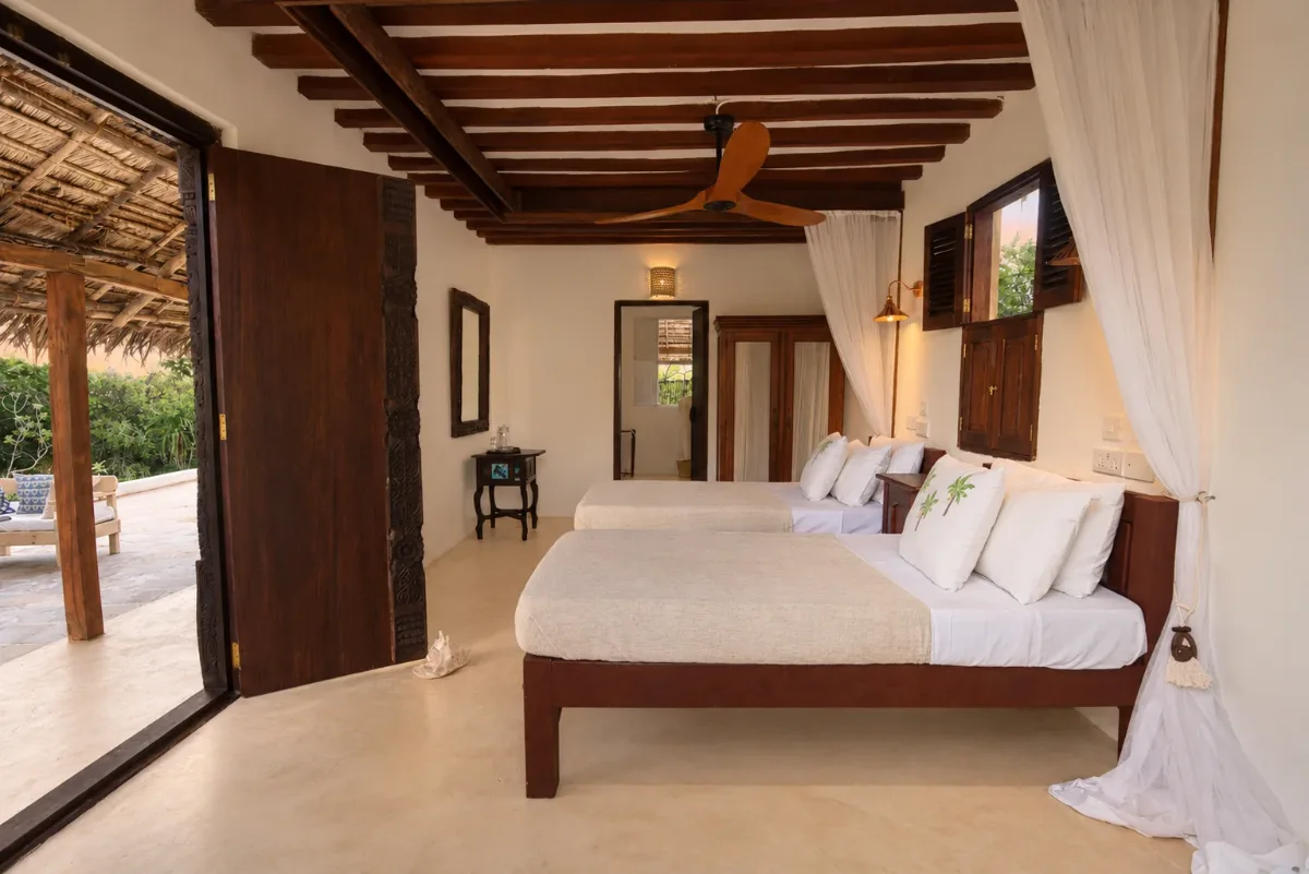 Mālama ground-floor bedroom, twin beds under nets with the carved door open to the terrace