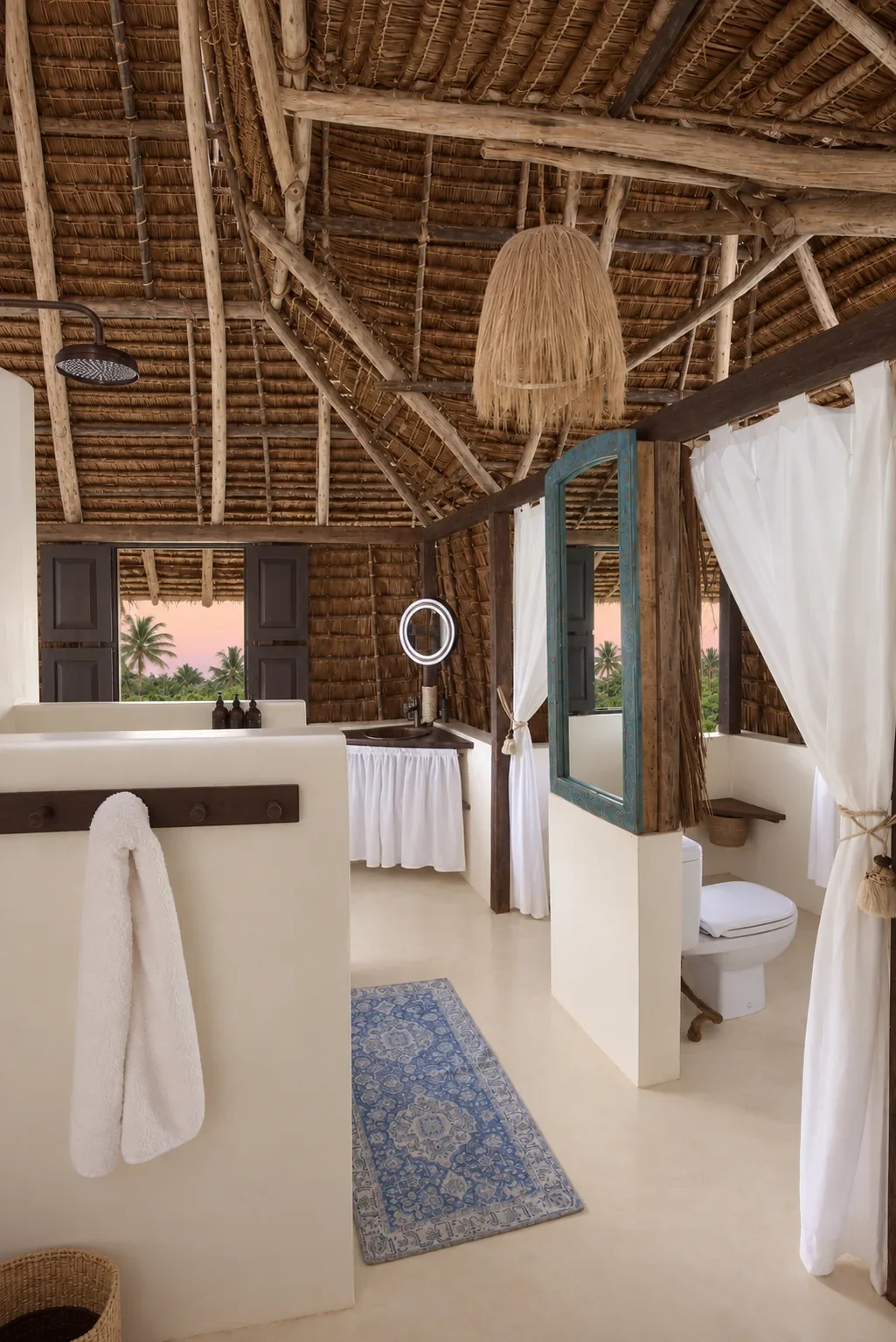The first-floor ensuite under makuti thatch, rain shower and a blue-framed mirror
