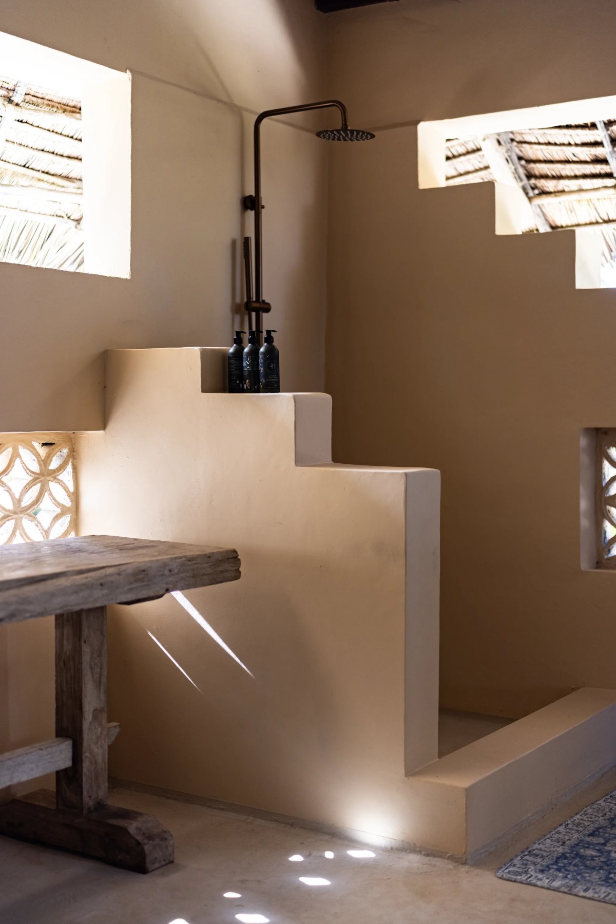 Moana cabana · stepped plaster shower with a brass rain head, light through the coral screen