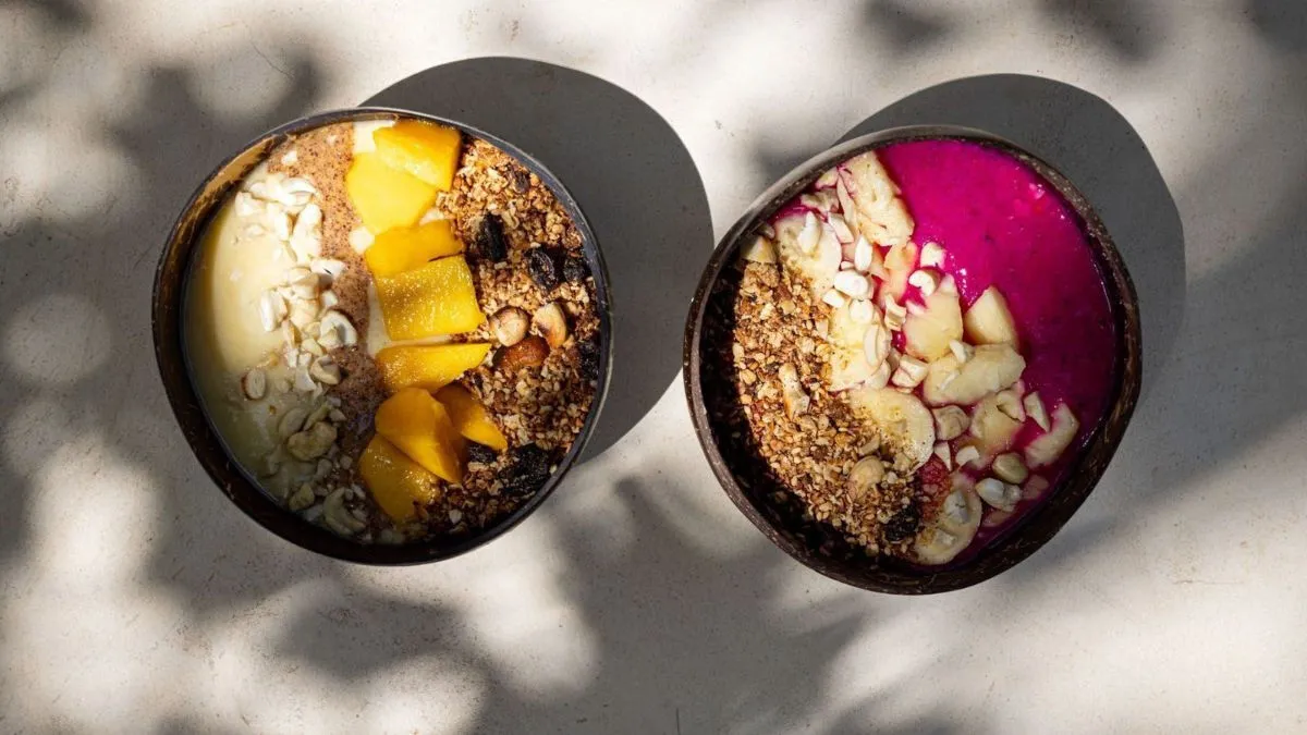 Two açaí bowls in coconut shells, topped with fruit, granola and coconut
