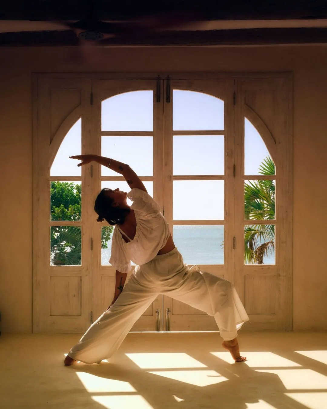 A yoga pose in front of arched windows looking out to the sea